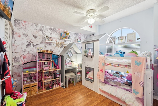bedroom featuring ceiling fan, wallpapered walls, a textured ceiling, and wood finished floors