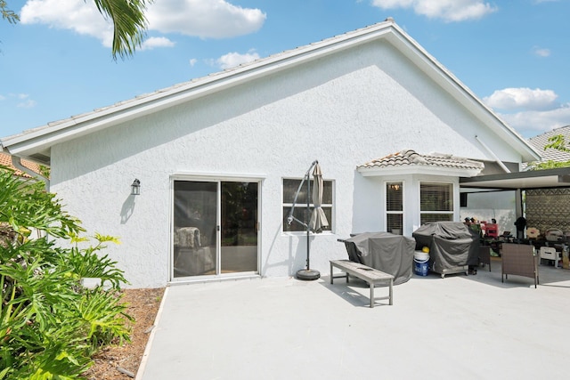 rear view of house featuring a tiled roof, a patio, and stucco siding