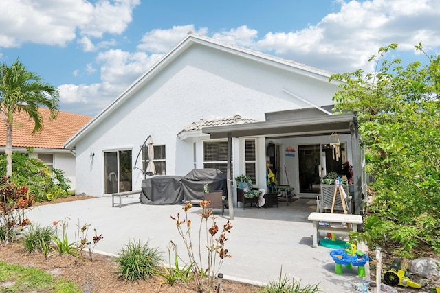 back of house featuring stucco siding, a patio area, and a tile roof