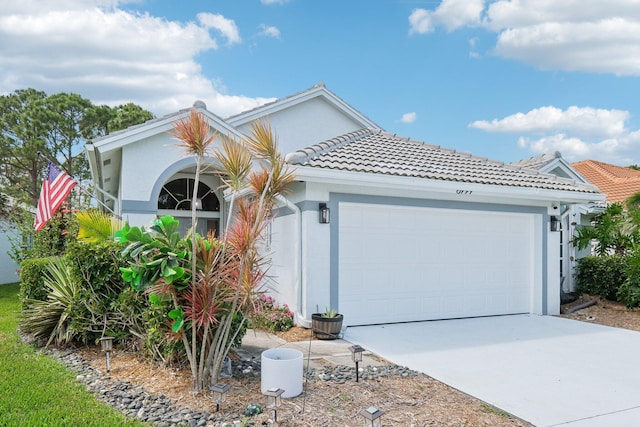 view of front of home featuring a tiled roof, a garage, stucco siding, and driveway