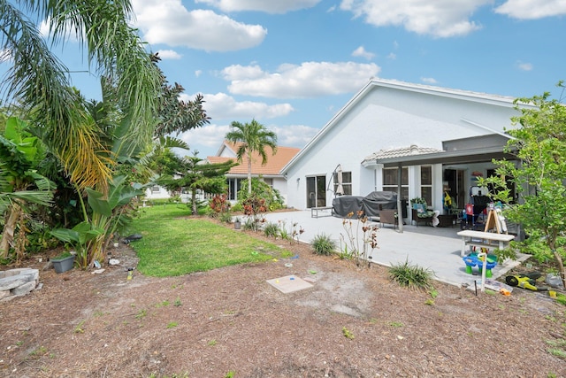 rear view of house featuring a lawn, a patio area, and stucco siding