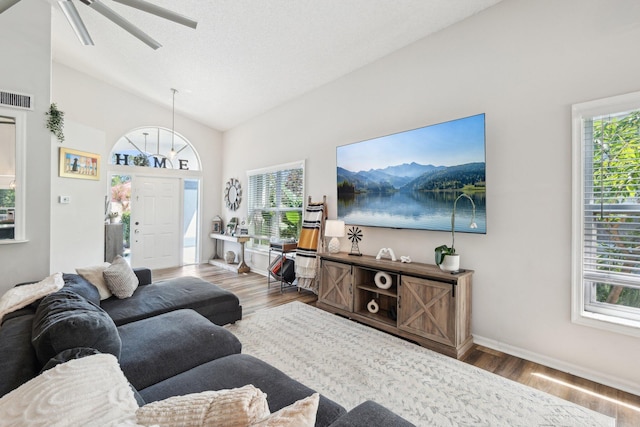 living area with visible vents, plenty of natural light, wood finished floors, and vaulted ceiling