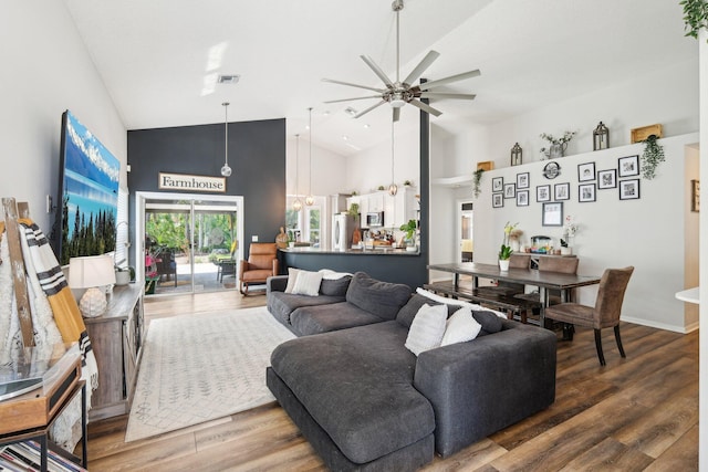 living room featuring high vaulted ceiling, ceiling fan with notable chandelier, baseboards, wood finished floors, and visible vents