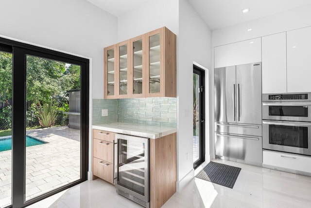 306 Plymouth Rd, West Palm Beach, FL 33405 - kitchen featuring glass insert cabinets, white cabinets, wine cooler, stainless steel appliances, and decorative backsplash