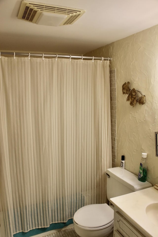 full bath featuring a textured wall, vanity, visible vents, and toilet