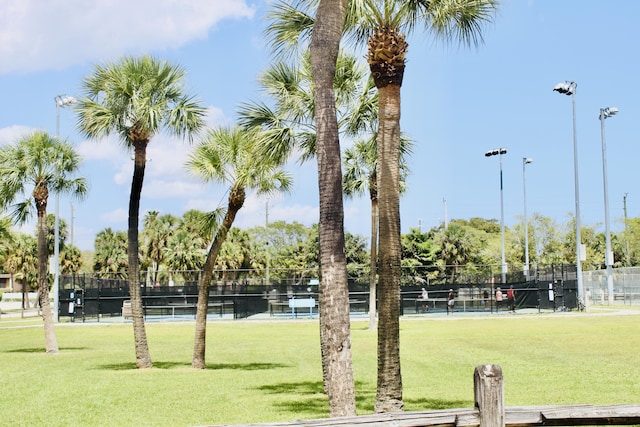 view of community with a tennis court, fence, and a lawn