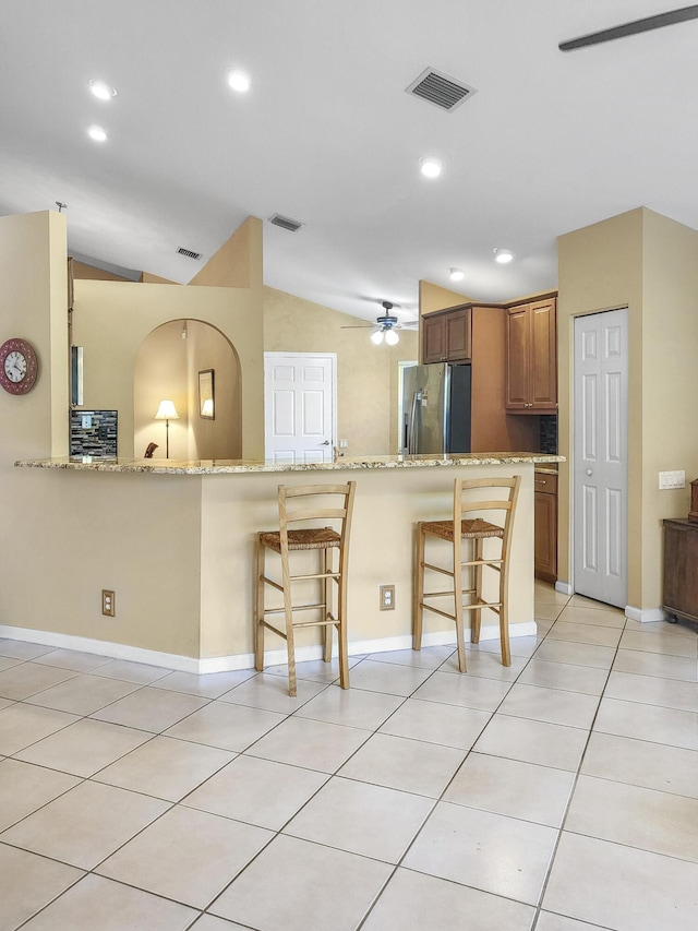 12404 Lakeridge Falls Dr, Boynton Beach, FL 33437 - kitchen with visible vents, a kitchen bar, light stone countertops, stainless steel fridge, and brown cabinetry