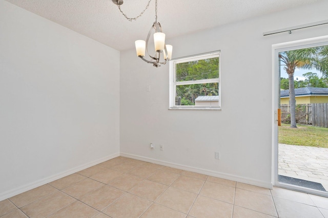spare room featuring baseboards, a textured ceiling, light tile patterned floors, and a chandelier