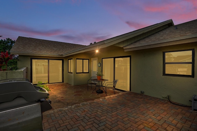 5680 Northpointe Ln, Boynton Beach, FL 33437 - back of property at dusk with a patio, a shingled roof, and stucco siding
