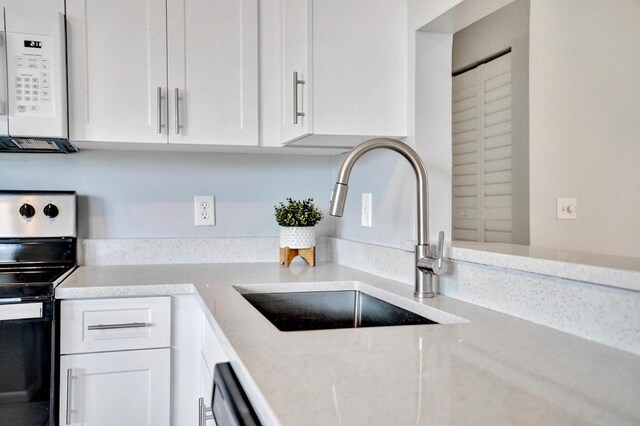 5680 Northpointe Ln, Boynton Beach, FL 33437 - kitchen with light stone countertops, white microwave, electric stove, white cabinetry, and a sink