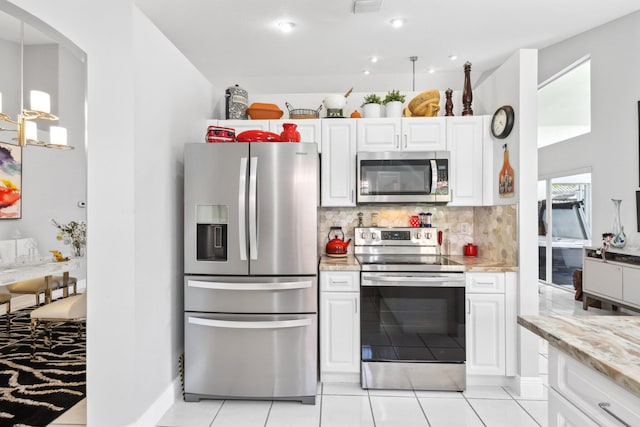 kitchen featuring arched walkways, white cabinetry, backsplash, appliances with stainless steel finishes, and light stone countertops