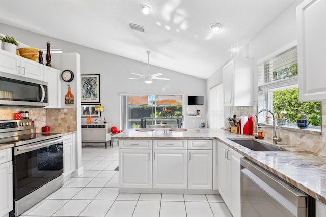 kitchen featuring lofted ceiling, stainless steel appliances, a sink, decorative backsplash, and a peninsula