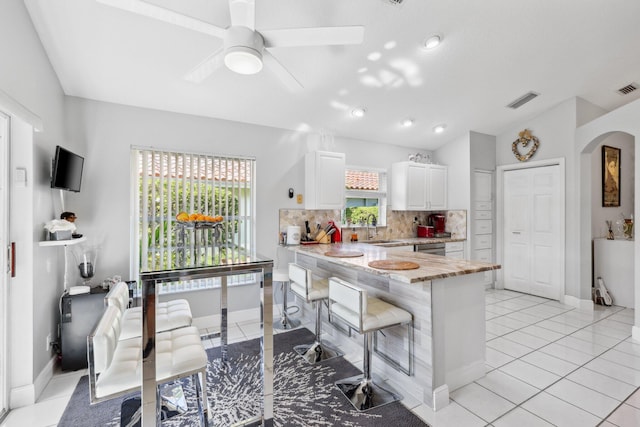kitchen featuring a sink, decorative backsplash, arched walkways, a peninsula, and white cabinetry
