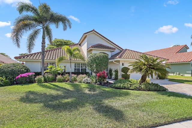 mediterranean / spanish home with a front lawn, driveway, a tiled roof, and stucco siding
