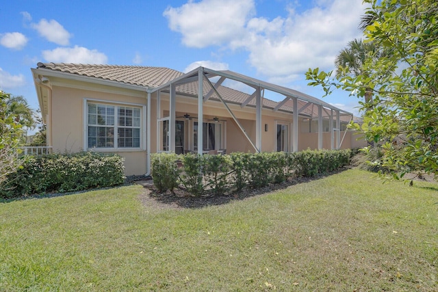 rear view of property featuring a ceiling fan, a lanai, stucco siding, and a yard