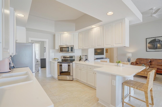 kitchen with a sink, white cabinets, a peninsula, a breakfast bar, and stainless steel appliances