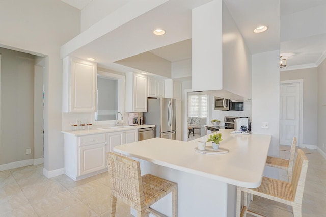 kitchen with white cabinets, appliances with stainless steel finishes, a breakfast bar, light countertops, and baseboards