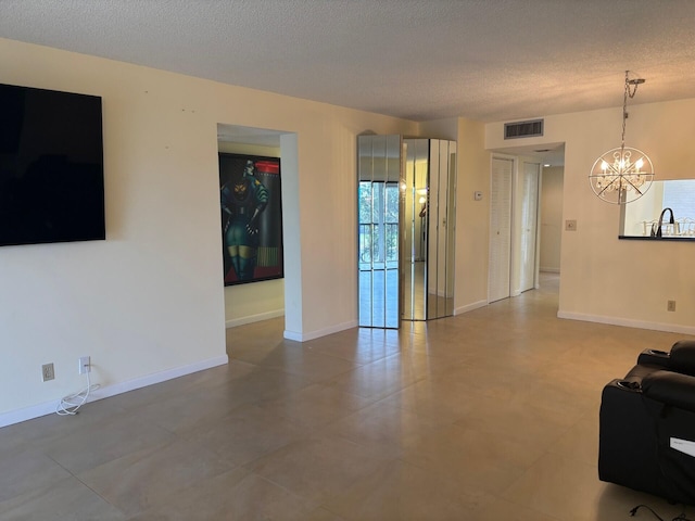 living room featuring a chandelier, a textured ceiling, visible vents, and baseboards