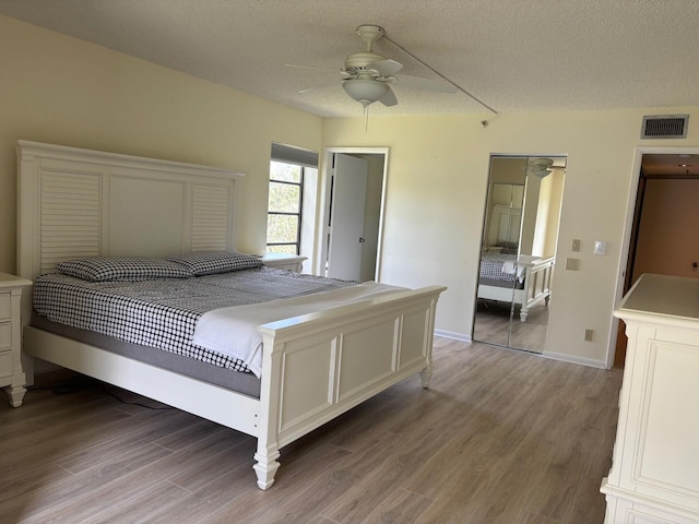 bedroom with a textured ceiling, baseboards, ceiling fan, visible vents, and wood finished floors