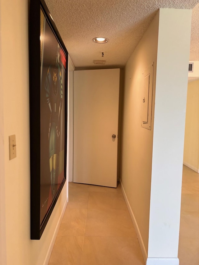 hallway with light tile patterned floors, a textured ceiling, visible vents, baseboards, and recessed lighting