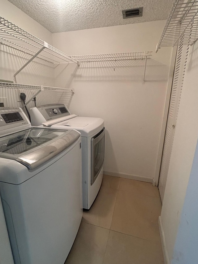 washroom featuring independent washer and dryer, light tile patterned floors, baseboards, visible vents, and laundry area