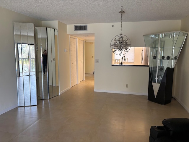 interior space featuring a textured ceiling, visible vents, baseboards, and a notable chandelier