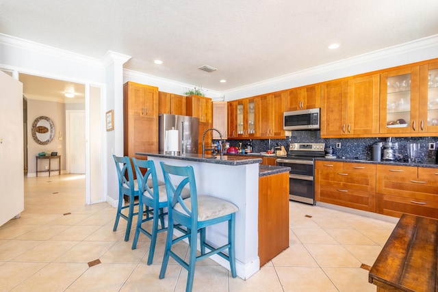 kitchen with brown cabinetry, ornamental molding, light tile patterned flooring, stainless steel appliances, and decorative backsplash