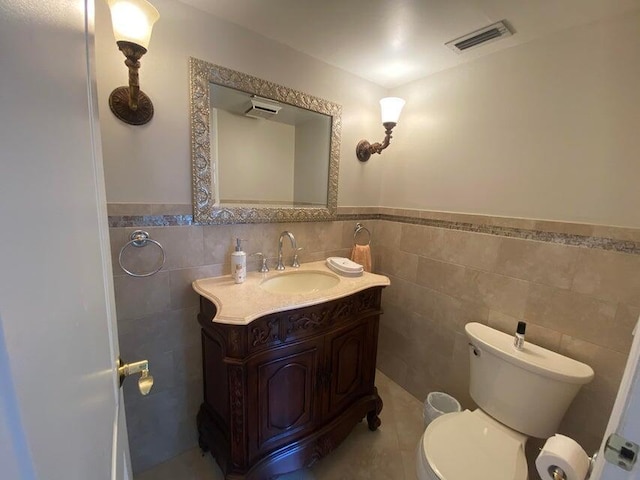 bathroom featuring toilet, vanity, visible vents, and tile walls