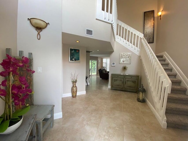 stairway with a high ceiling, baseboards, tile patterned floors, and visible vents