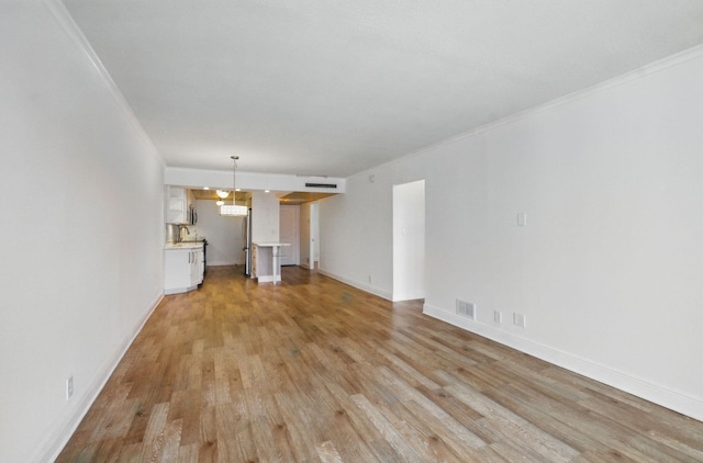 unfurnished living room with baseboards, light wood-style flooring, visible vents, and crown molding