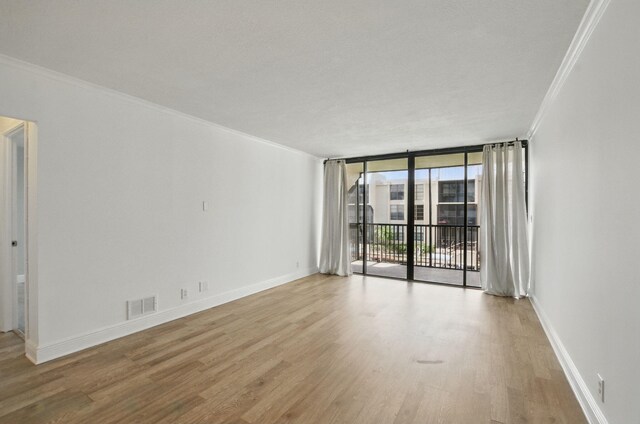 spare room with wood finished floors, visible vents, crown molding, and baseboards