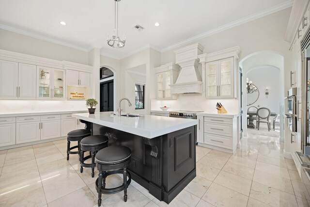 9650 Eden Mnr, Parkland, FL 33076 - kitchen featuring crown molding, a sink, light countertops, arched walkways, and a kitchen island with sink