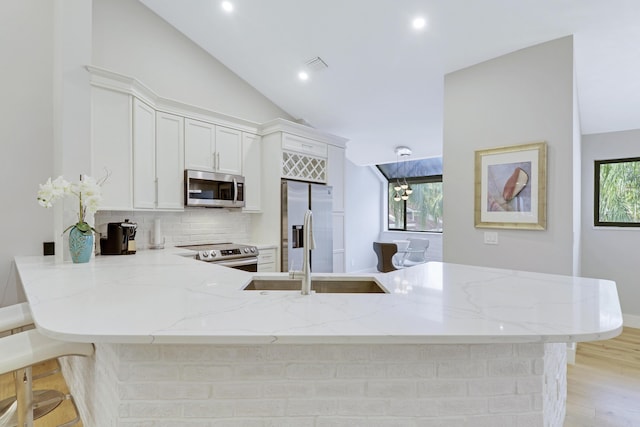 kitchen featuring stainless steel appliances, a peninsula, a sink, decorative backsplash, and light stone counters