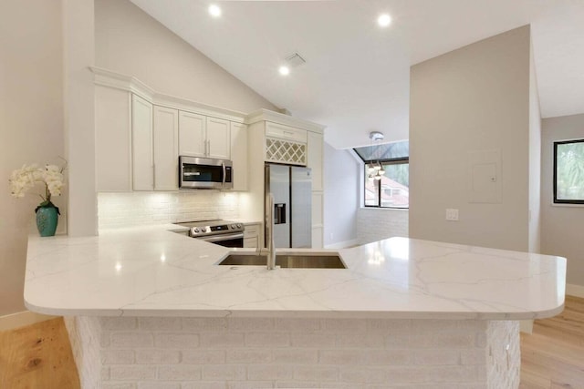kitchen with decorative backsplash, a peninsula, light stone countertops, and stainless steel appliances