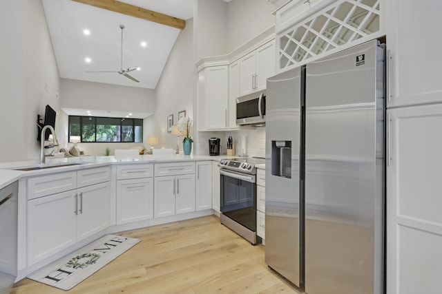 kitchen with light wood finished floors, stainless steel appliances, a sink, white cabinetry, and high vaulted ceiling