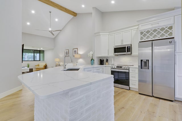 kitchen featuring a peninsula, a sink, light stone countertops, high vaulted ceiling, and appliances with stainless steel finishes