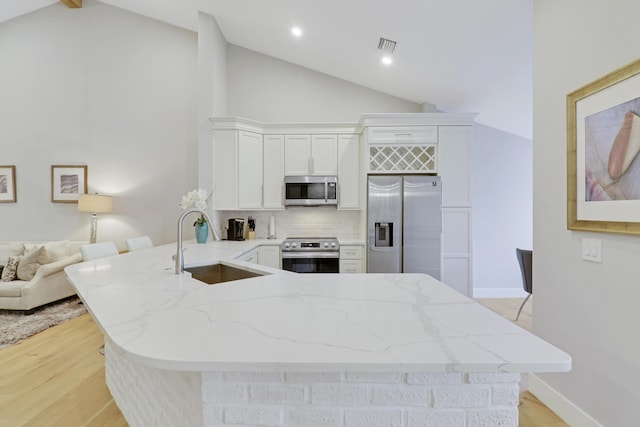 kitchen featuring stainless steel appliances, a sink, light wood-type flooring, decorative backsplash, and a peninsula