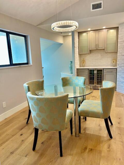 dining area with wine cooler, light wood-style flooring, vaulted ceiling, baseboards, and visible vents