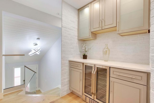 bar with tasteful backsplash, light wood-type flooring, beverage cooler, and baseboards