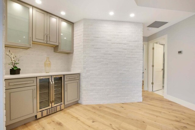 bar with a bar, decorative backsplash, beverage cooler, light wood-style floors, and baseboards