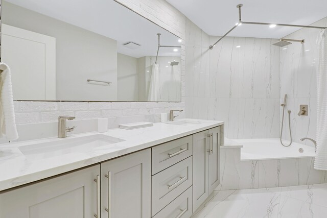bathroom featuring a combined bath / shower with marble appearance, a sink, double vanity, and tile walls