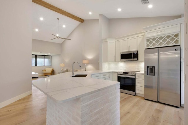kitchen featuring a peninsula, a sink, light stone countertops, high vaulted ceiling, and appliances with stainless steel finishes