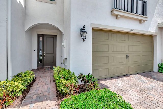 property entrance with an attached garage, stucco siding, and decorative driveway