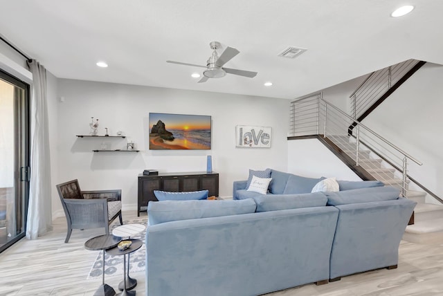 living room with wood finished floors, visible vents, stairs, and ceiling fan