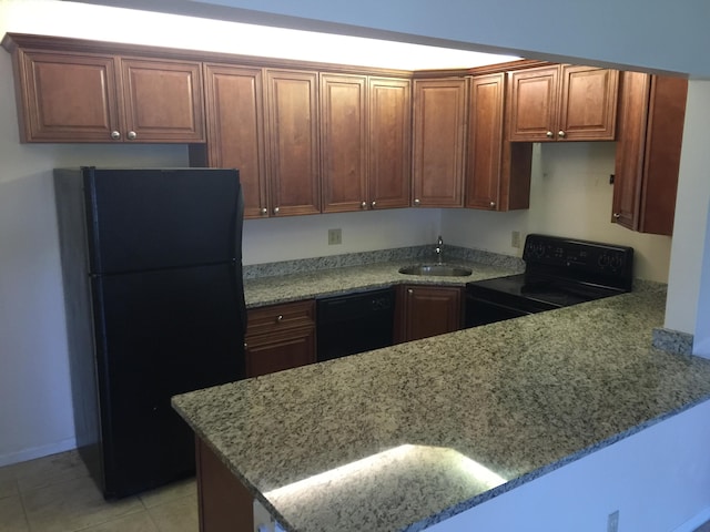 kitchen with a sink, a peninsula, black appliances, light tile patterned flooring, and light stone counters