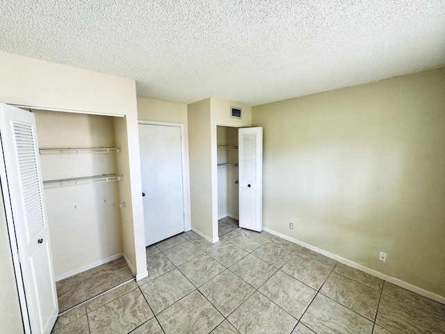 unfurnished bedroom featuring a textured ceiling, light tile patterned floors, baseboards, and visible vents
