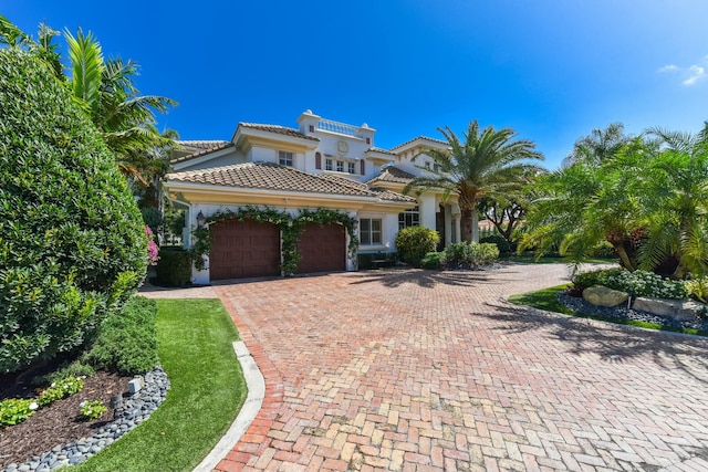 mediterranean / spanish-style home featuring a tile roof, decorative driveway, a garage, and stucco siding