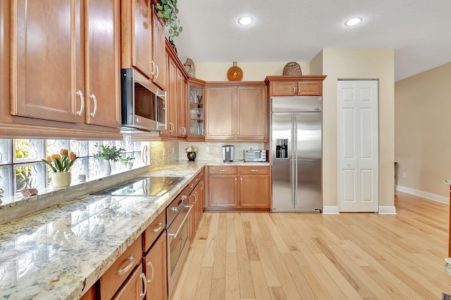 9380 Isles Cay Dr, Delray Beach, FL 33446 - kitchen with appliances with stainless steel finishes, light stone counters, tasteful backsplash, brown cabinetry, and light wood-style flooring