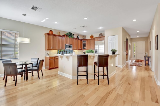 9380 Isles Cay Dr, Delray Beach, FL 33446 - kitchen featuring stainless steel appliances, brown cabinets, light wood finished floors, a kitchen bar, and recessed lighting