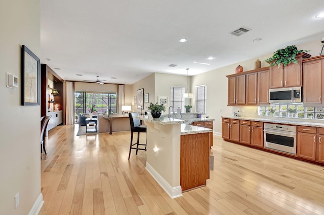 9380 Isles Cay Dr, Delray Beach, FL 33446 - kitchen with stainless steel appliances, a kitchen breakfast bar, brown cabinetry, light wood-style flooring, and recessed lighting